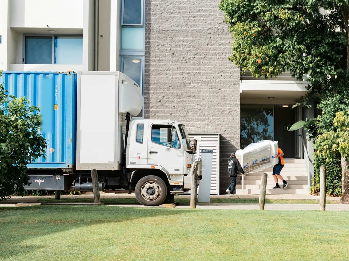 Movers carrying a wrapped sofa from a moving truck into an apartment building